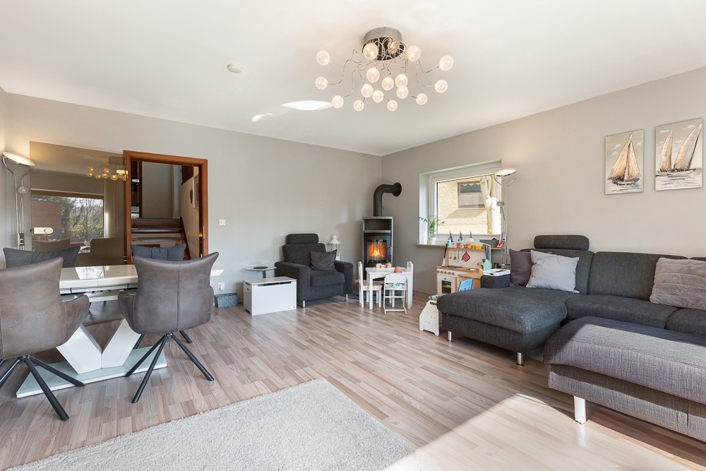 Helles Wohnzimmer mit Ecksofa, Kamin, Essbereich, Spielzeugküche und moderner Deckenleuchte.
