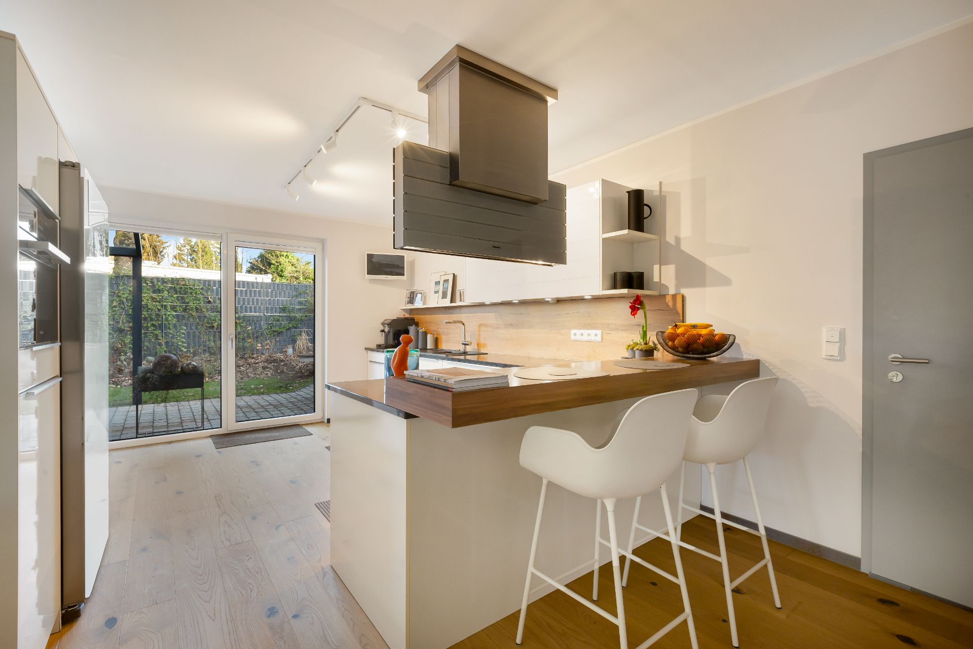 Moderne Küche mit Kochinsel, zwei weißen Barhockern und großem Fenster zum Garten.