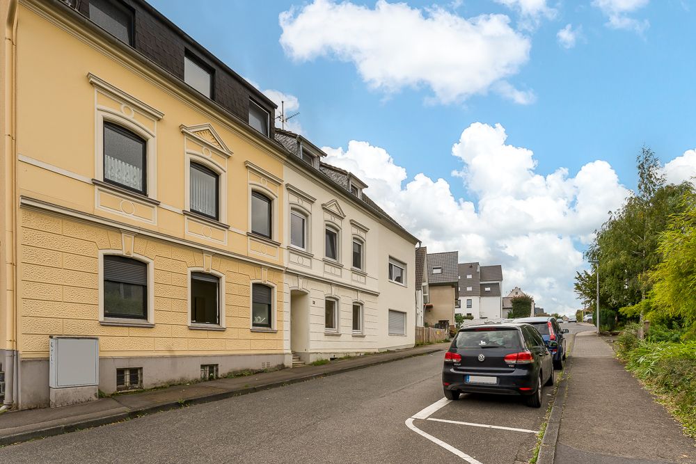 Wohnhäuser an einer ruhigen Straße mit parkenden Autos und Gehweg bei Tageslicht.
