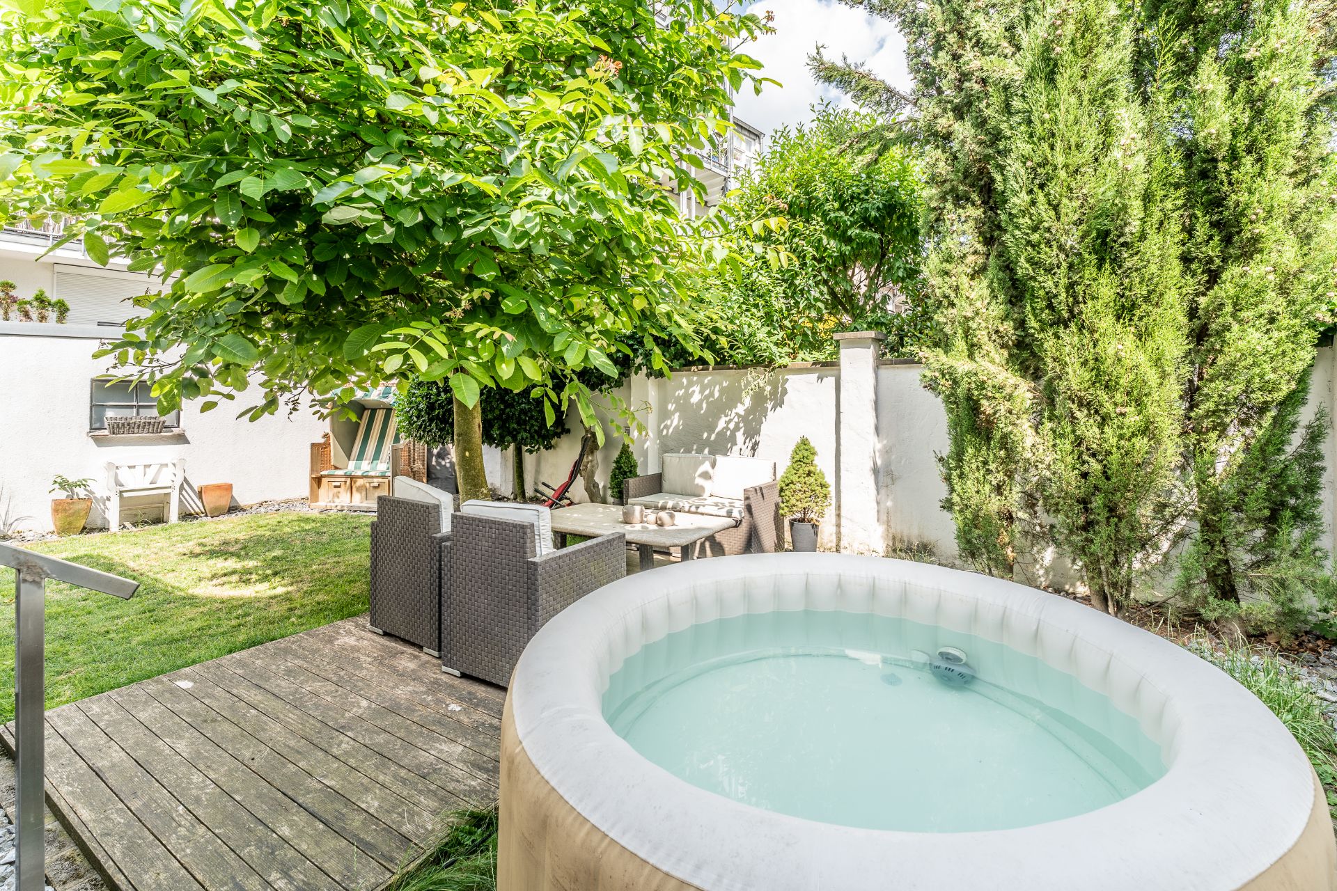 Garten mit aufblasbarem Pool, Holzdielen, Sitzgruppe und viel grüner Bepflanzung.