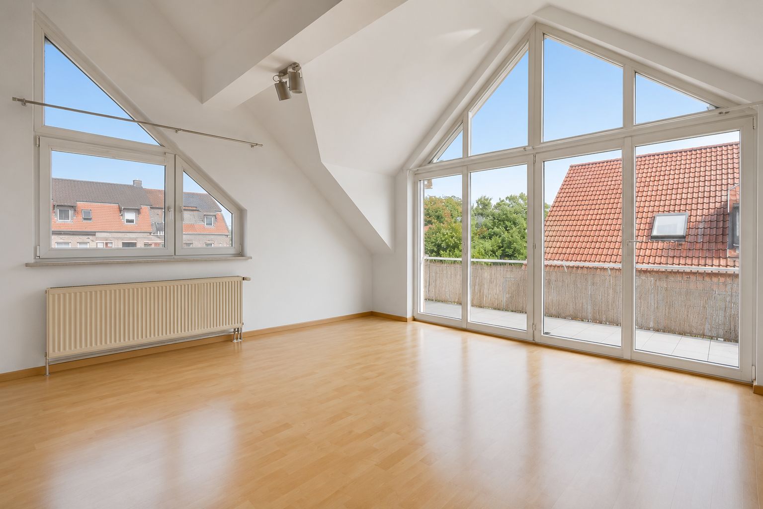 Helles Wohnzimmer mit großen Fenstern, Parkettboden und Zugang zu einem Balkon.