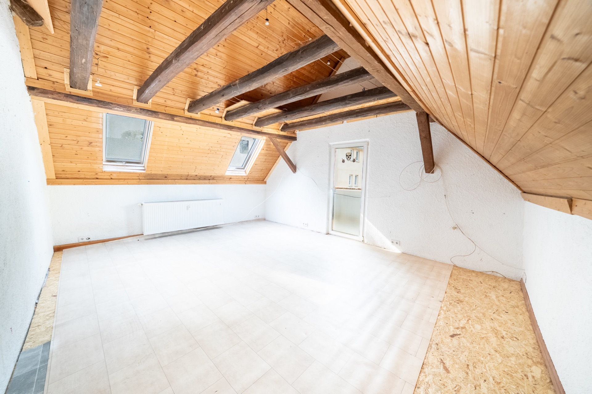 Heller Dachraum mit sichtbaren Holzbalken, zwei Dachfenstern und Holzwänden.
