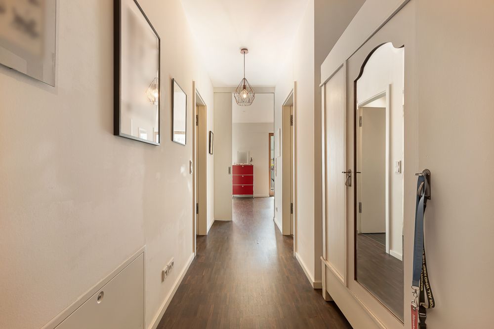 Heller Flur mit Holzboden, Wandbildern und einem weißen Spiegel-Schrank.