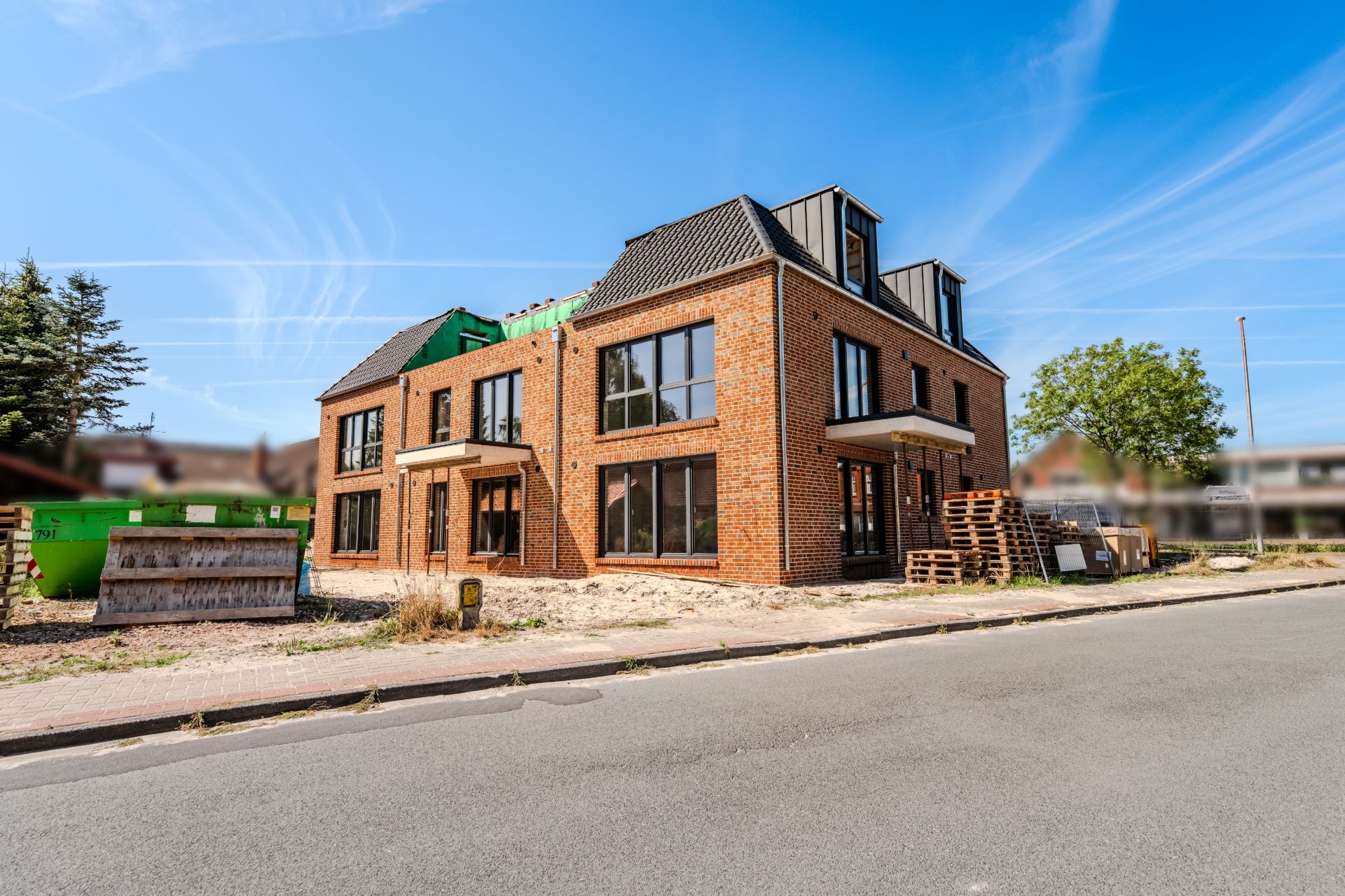 Neues, modernes Backsteinhaus mit großen Fenstern an einer ruhigen Straße, Baumaterialien davor.