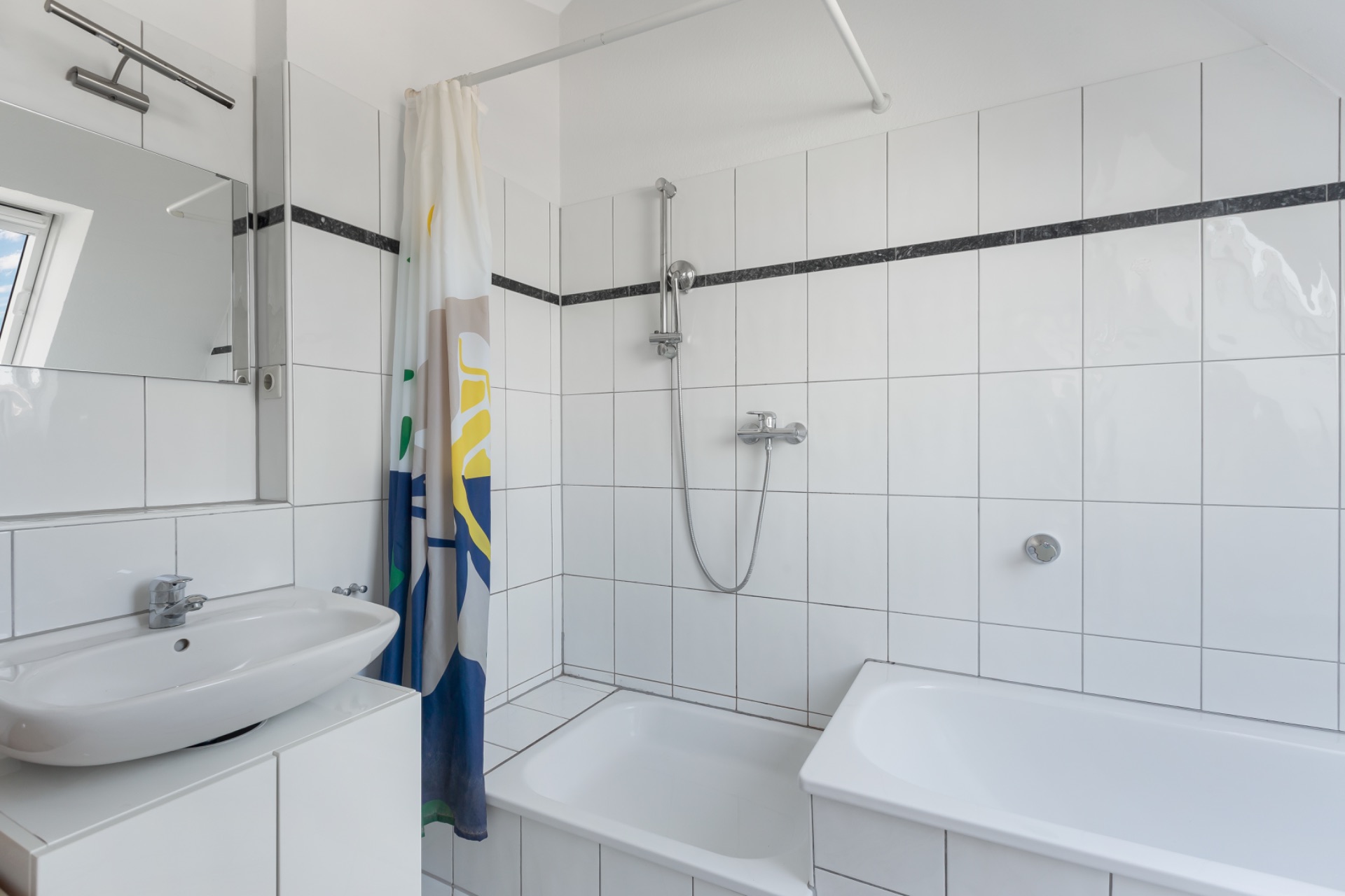 Helles Badezimmer mit Waschbecken, Spiegel, Badewanne und Dusche mit Duschvorhang.