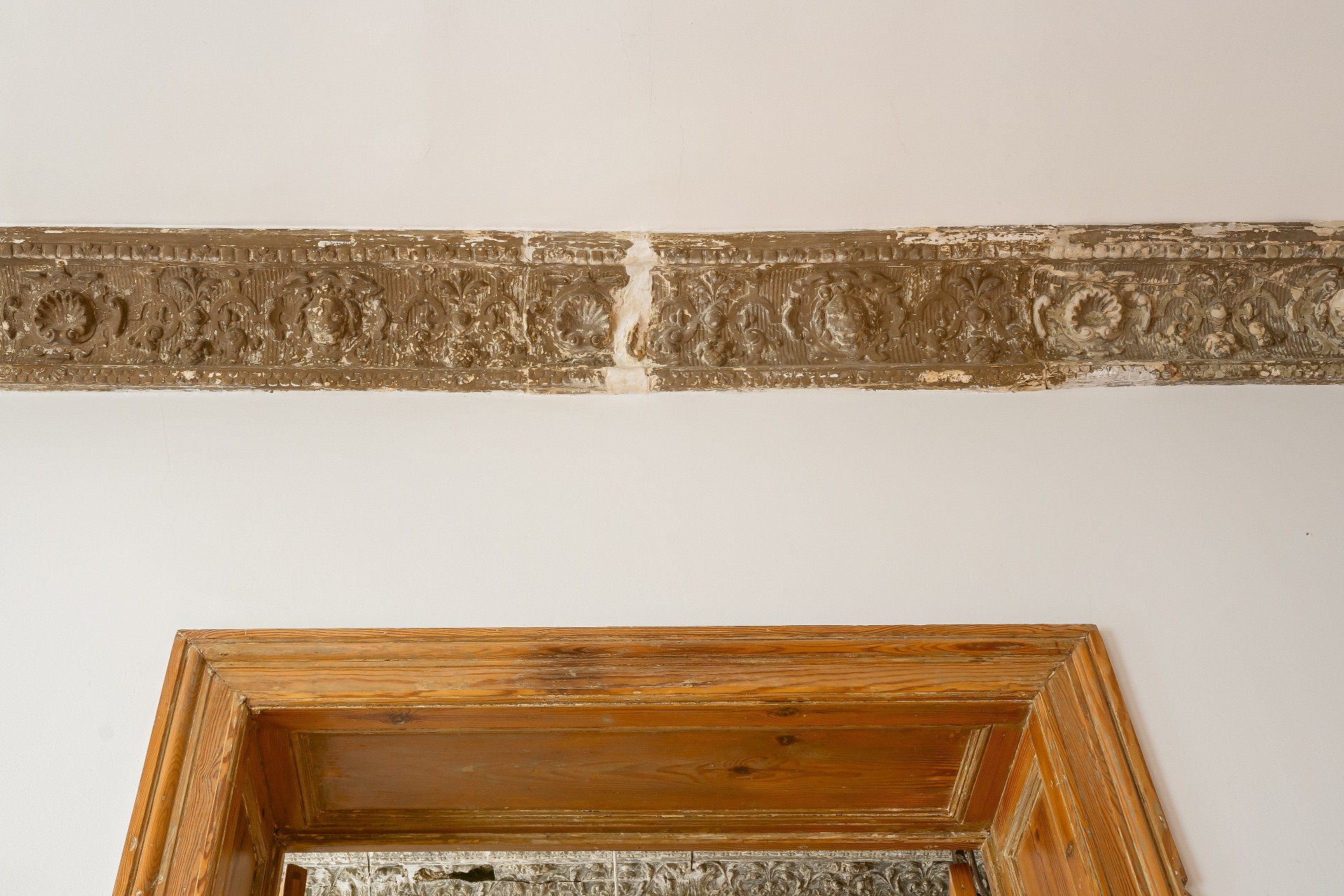 Oberer Teil eines Türrahmens aus Holz und eine verzierte Stuckleiste an der Wand.