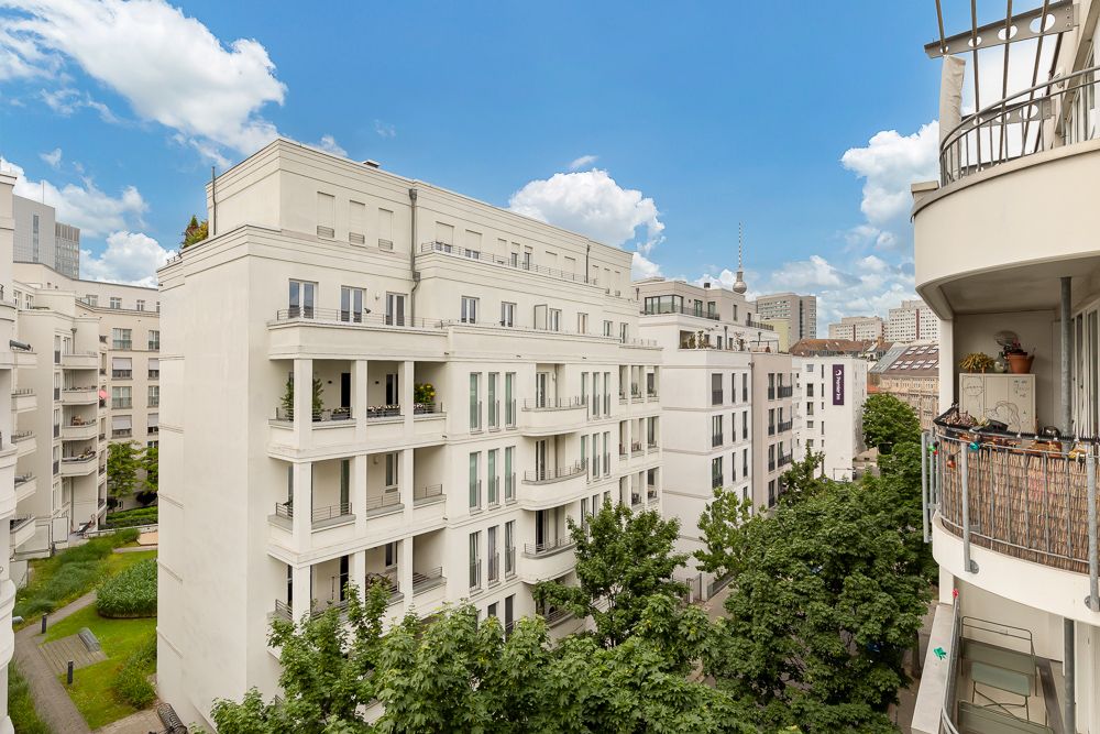 Blick auf moderne Wohnhäuser mit Balkonen und grünen Bäumen im Innenhof bei blauem Himmel.