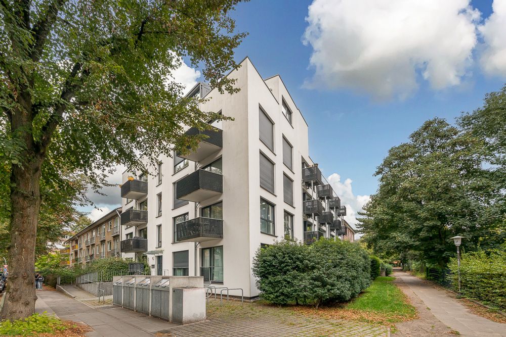 Modernes Wohnhaus mit Balkonen an der Straßenecke, umgeben von Bäumen und Gehwegen.