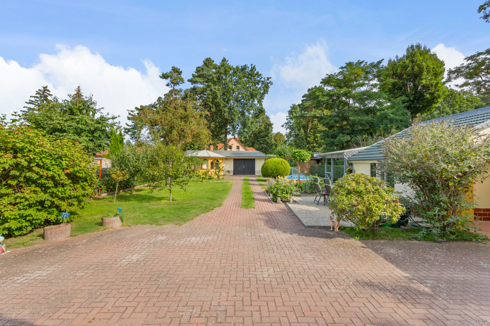 Gepflasterte Einfahrt mit Garten, Bäumen und Garage im Hintergrund.