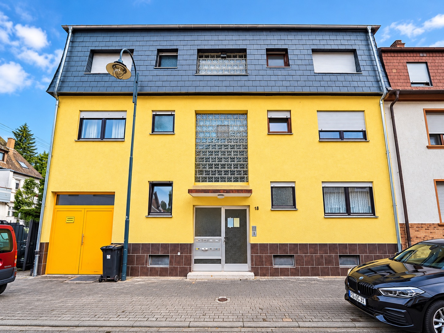 Gelbes Wohnhaus mit brauner Fassade im Erdgeschoss und mehreren Fenstern, Eingangstür mittig.