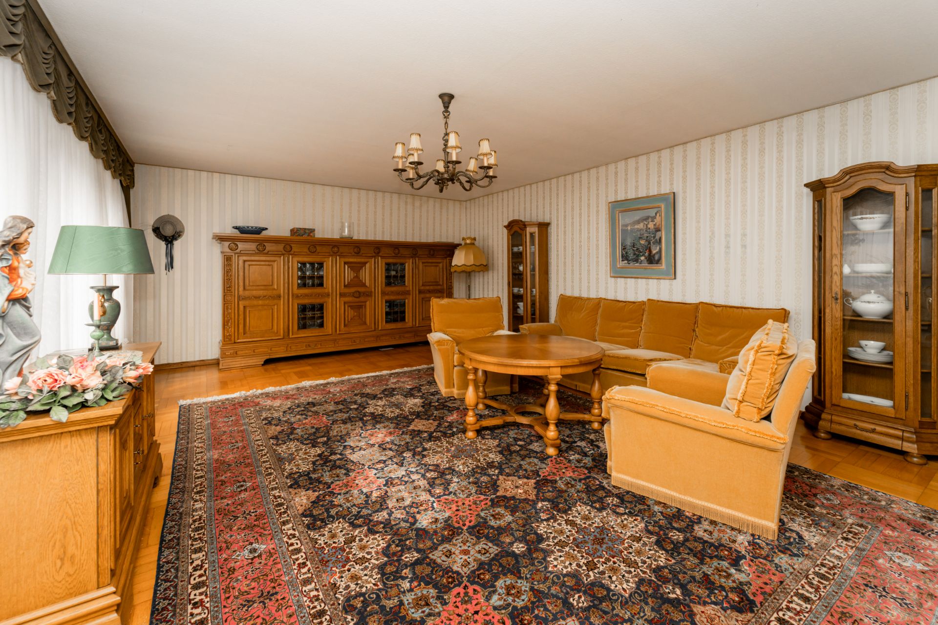 Wohnzimmer mit großem Teppich, gelbem Sofa, Holzmöbeln und Kronleuchter.