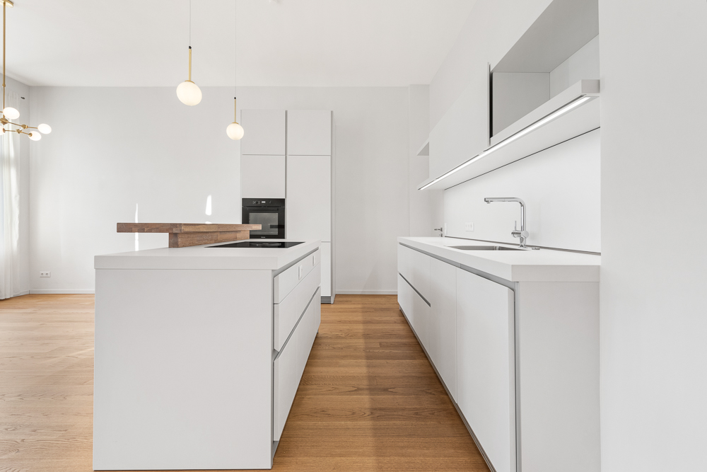 Moderne weiße Küche mit Kochinsel, Holzboden und minimalistischer Beleuchtung.
