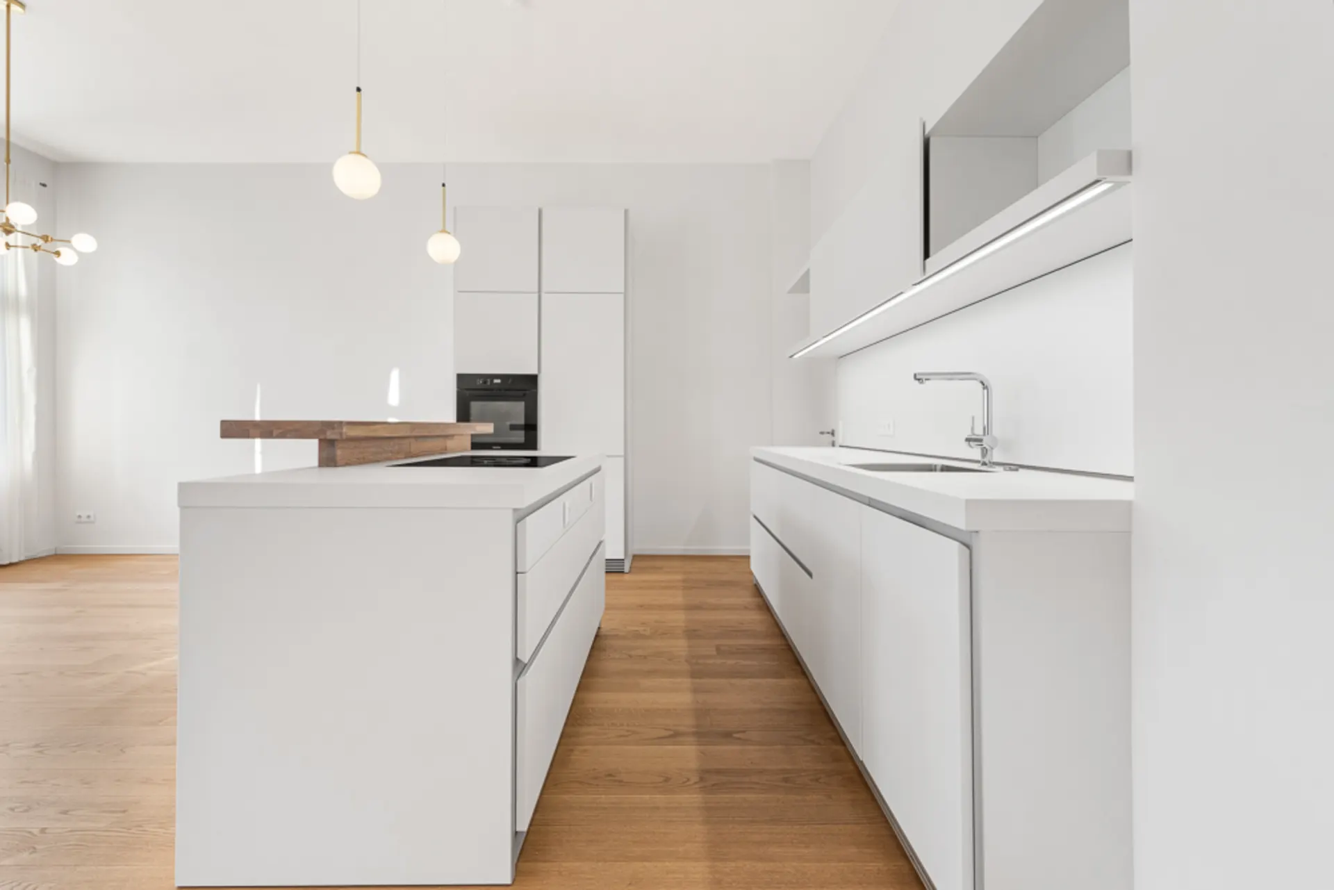 Moderne weiße Küche mit Kochinsel, Holzboden und minimalistischer Beleuchtung.