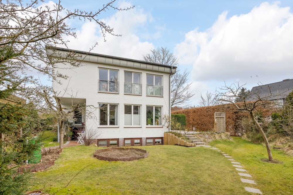 Weißes Einfamilienhaus mit großen Fenstern und gepflegtem Garten im Vordergrund.