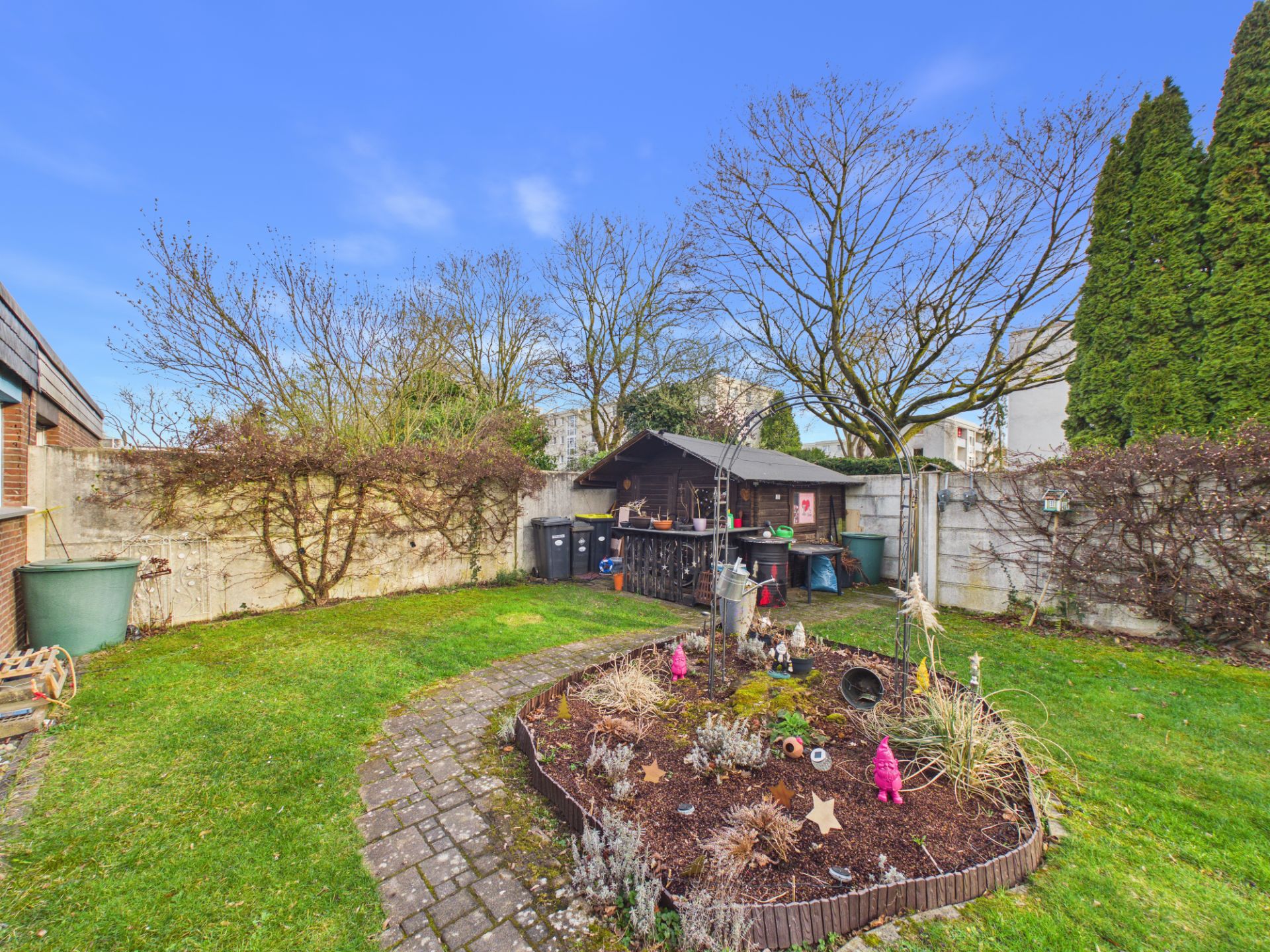 Garten mit Rasen, Beet in der Mitte und Gartenschuppen im Hintergrund.