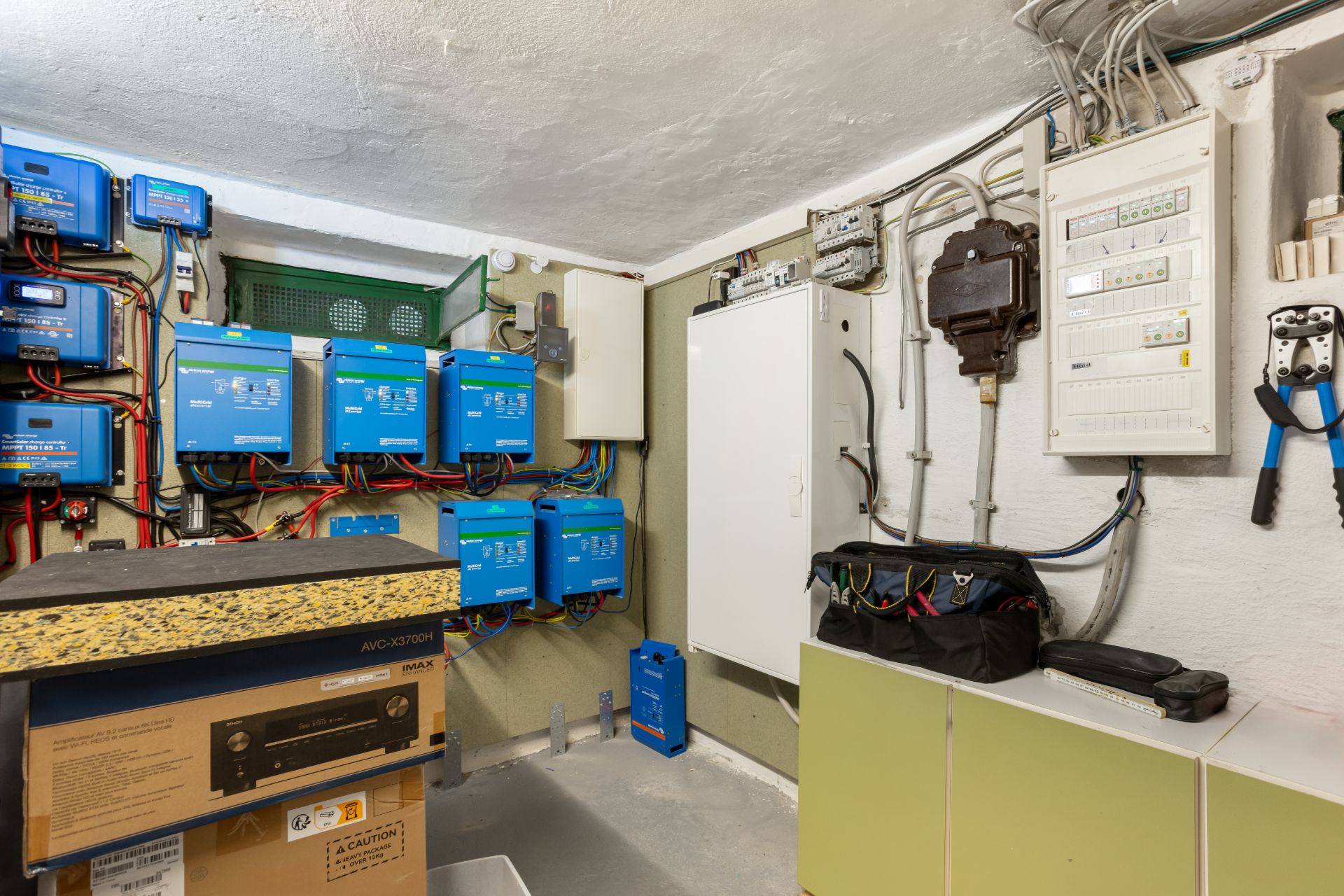 Hauswirtschaftsraum mit mehreren blauen Stromwechselrichtern und Verteilerschränken an der Wand.