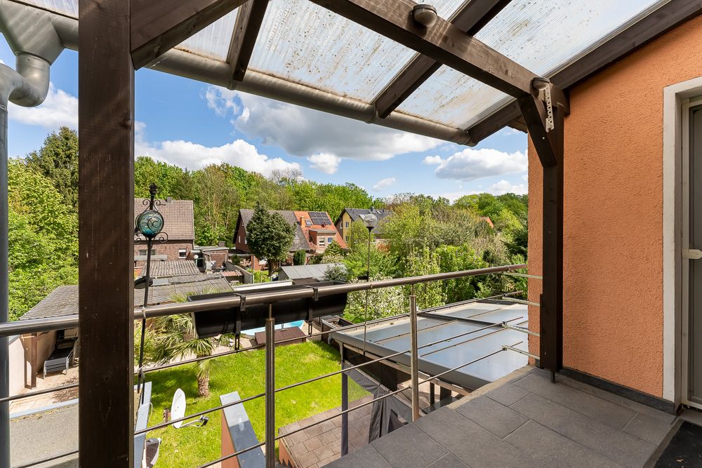 Überdachter Balkon mit Blick auf einen grünen Garten und benachbarte Häuser.
