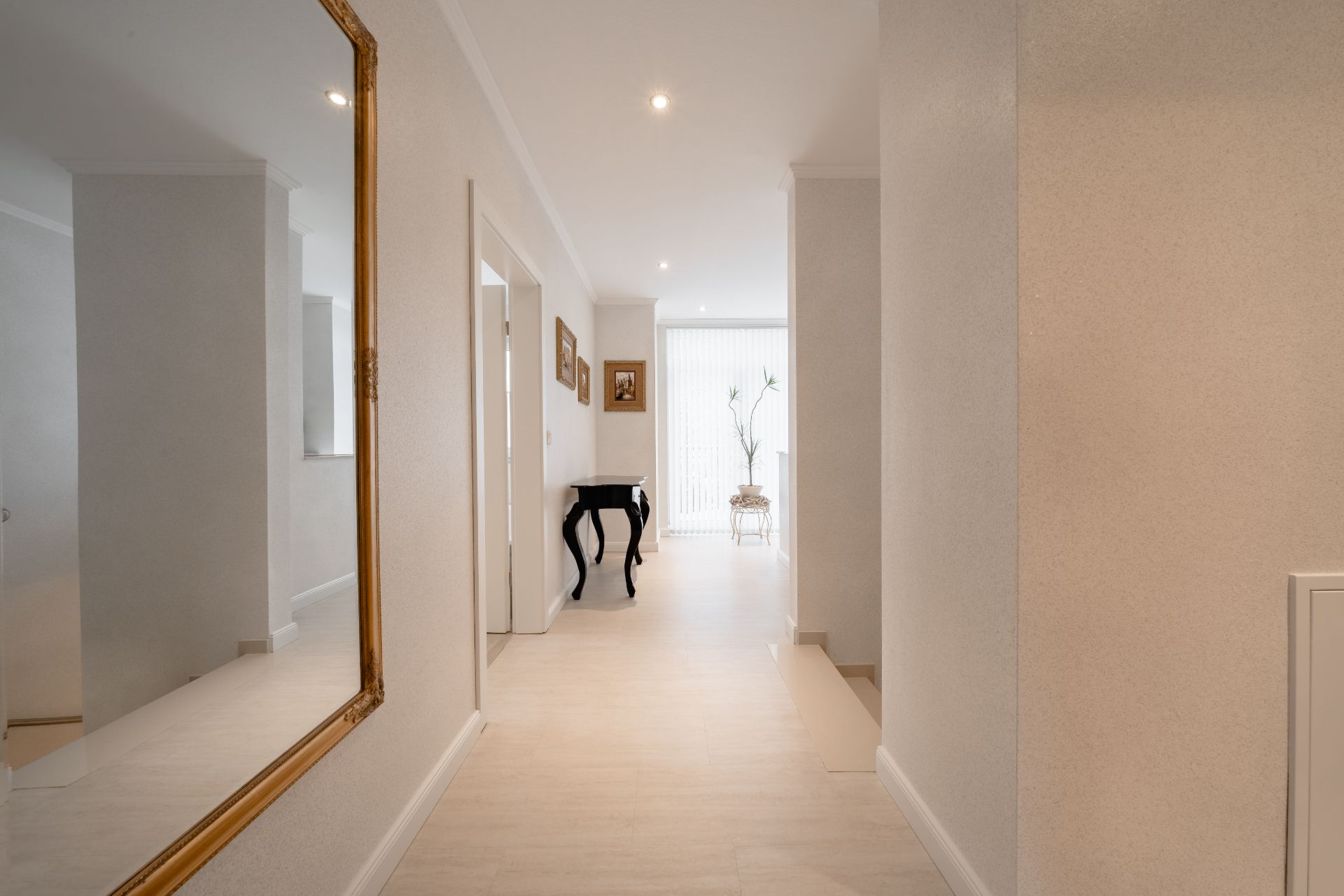 Heller Flur mit großem Spiegel, Bildern an der Wand und einem kleinen Tisch am Ende.