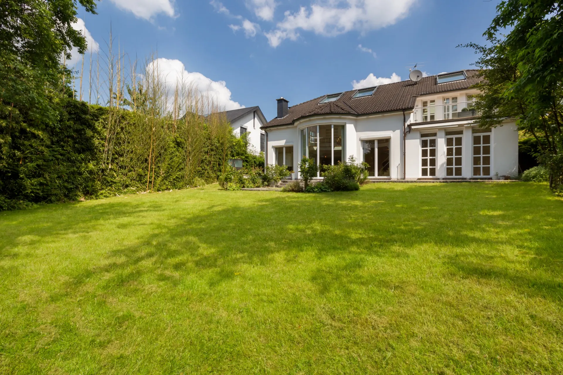 Gepflegter Garten mit Rasenfläche und Blick auf ein modernes Wohnhaus mit großen Fenstern.