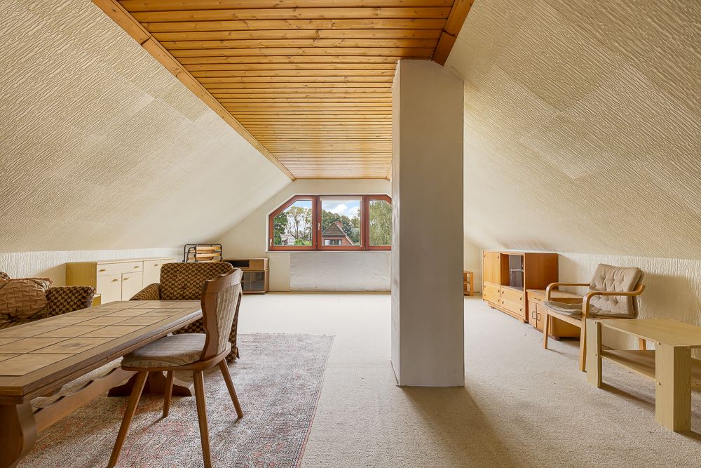 Heller Dachbodenraum mit Holzdecke, Fenstern, Tisch, Stühlen und Schränken.