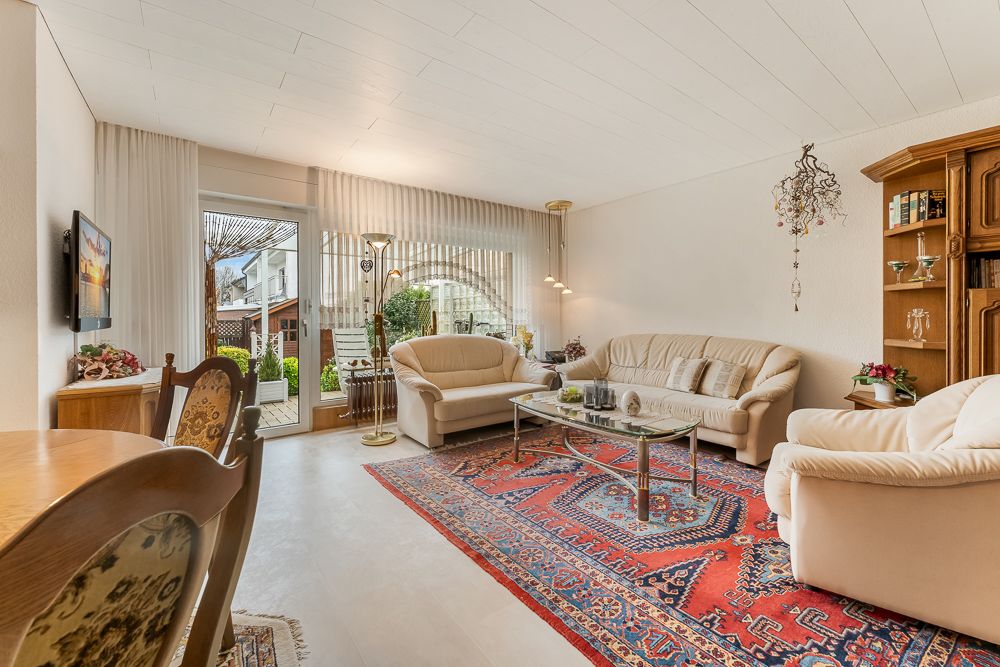 Helles Wohnzimmer mit Teppich, beigen Sofas, Glastisch und Zugang zur Terrasse.