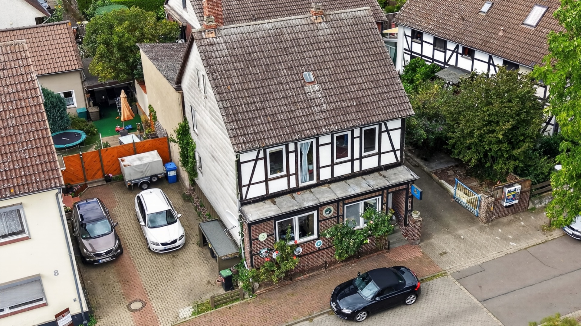 Zweistöckiges Fachwerkhaus mit Vorgarten, parkenden Autos und Nachbarhäusern.
