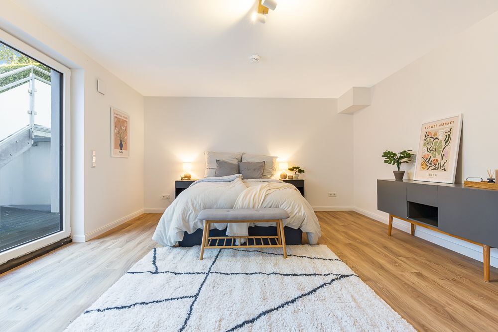 Helles Schlafzimmer mit Doppelbett, Teppich, Nachttischen und großem Fenster zum Außenbereich.