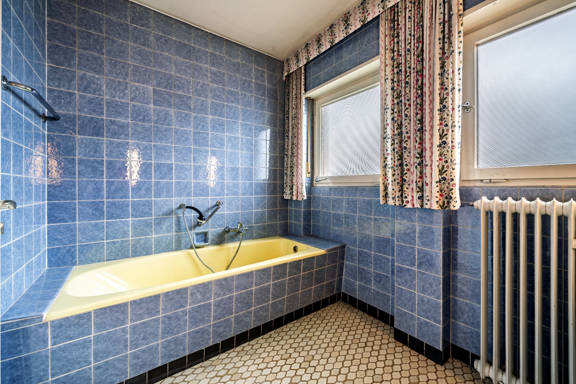 Badezimmer mit blauer Fliesenwand, gelber Badewanne, Fenstern und Heizkörper.
