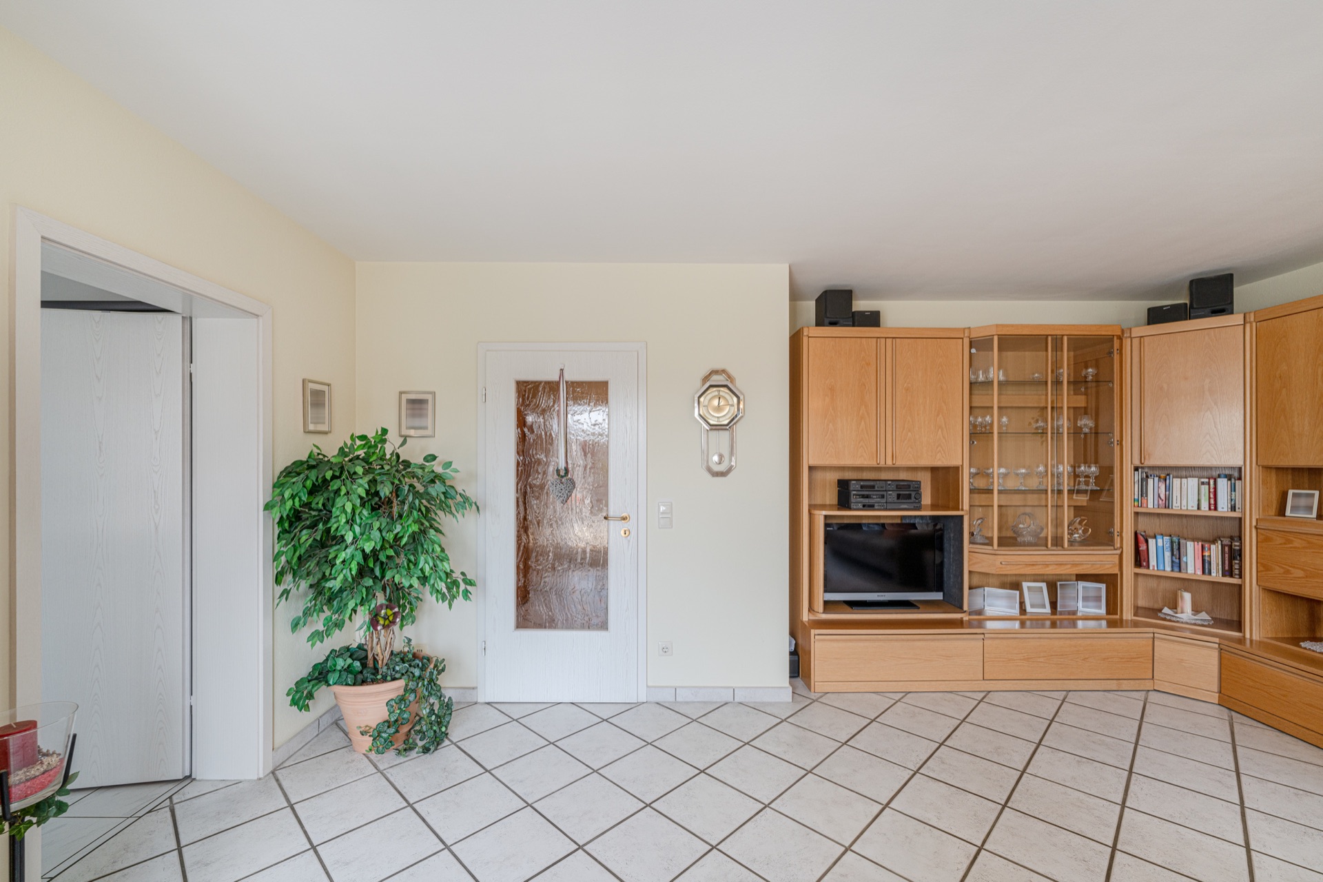 Wohnzimmer mit großer Holzschrankwand, Fernseher, Pflanze und Glastür.