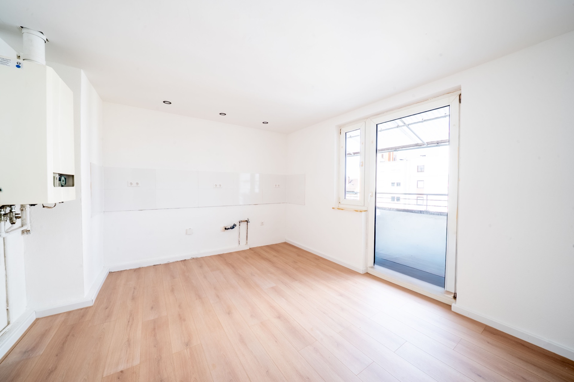 Leerer, heller Raum mit Holzfußboden, weißen Wänden und Zugang zu einem Balkon.