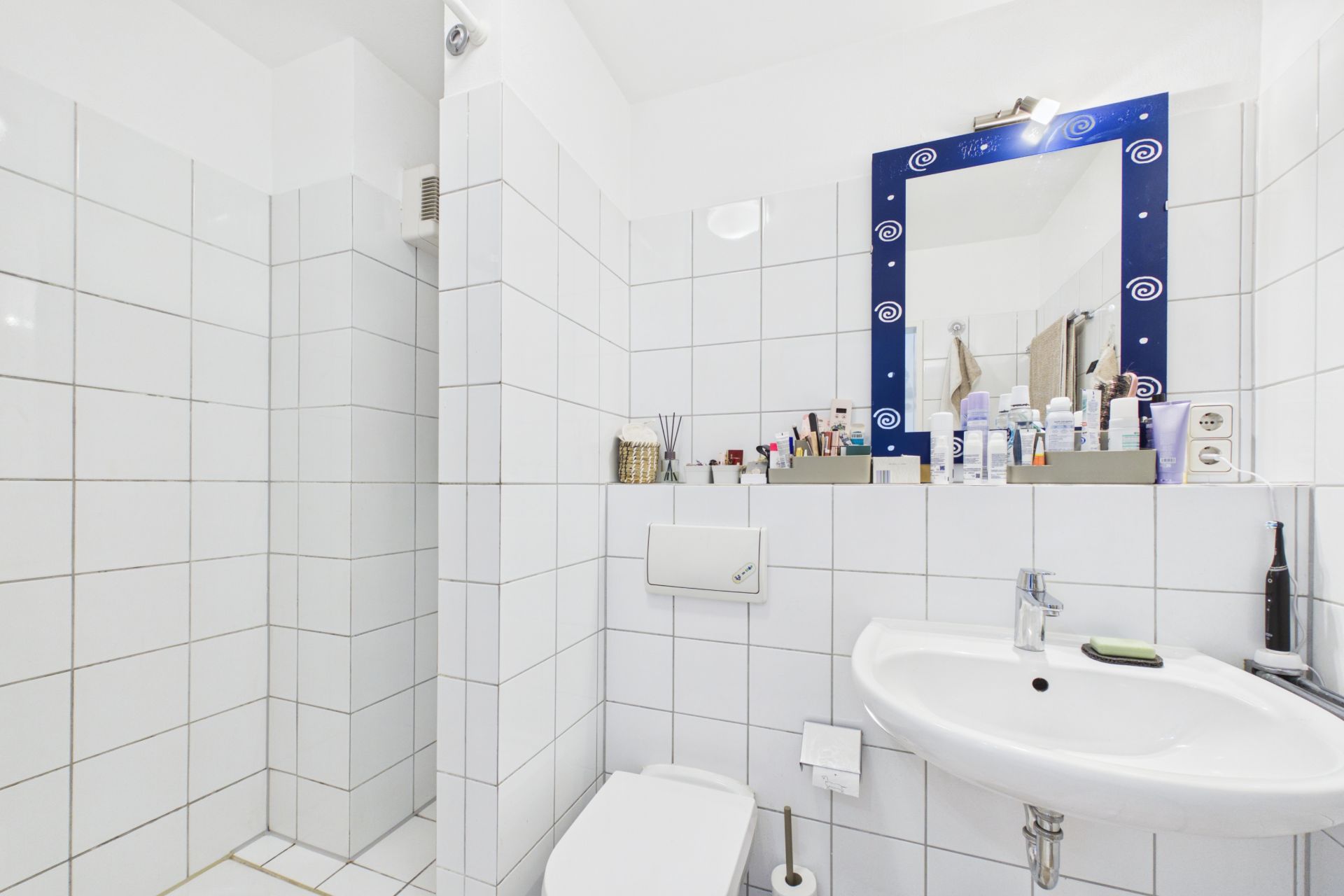 Modernes, weiß gefliestes Badezimmer mit Dusche, Toilette und Waschbecken.