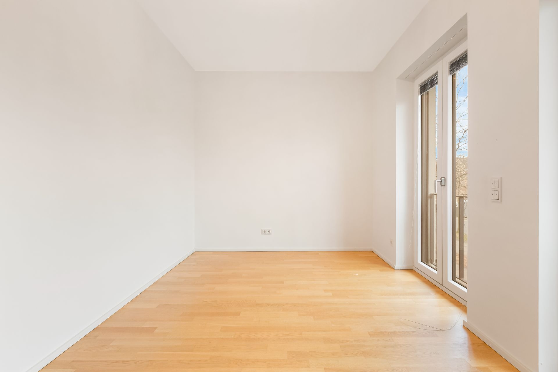 Heller leerer Raum mit Holzfußboden und bodentiefen Fenstern.