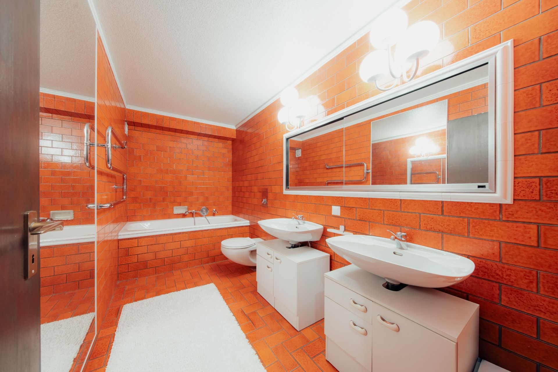 Modernes Badezimmer mit orangefarbenen Fliesen, zwei Waschbecken, Badewanne und großem Spiegel.