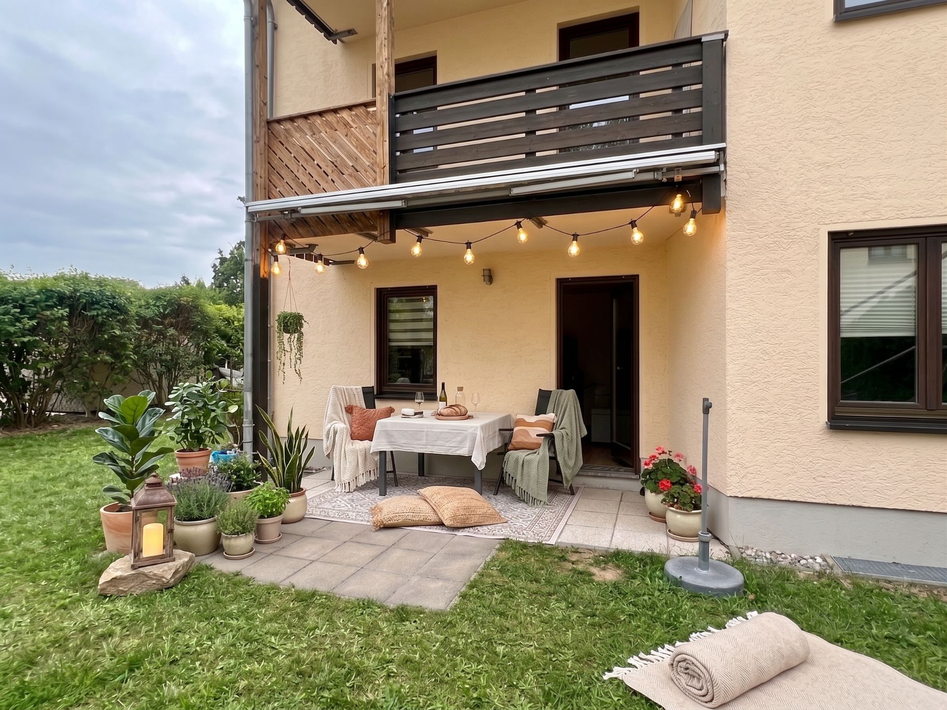 Überdachte Terrasse mit Tisch, Stühlen, Lichterkette und vielen Pflanzen im Garten.