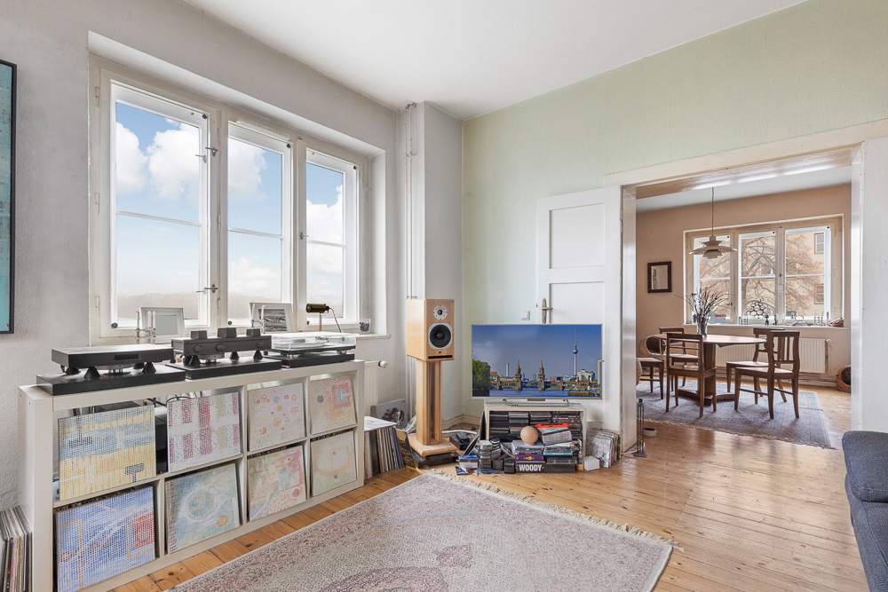 Helles Wohnzimmer mit großen Fenstern, Plattenspielern, Regalen und Blick auf ein Esszimmer.