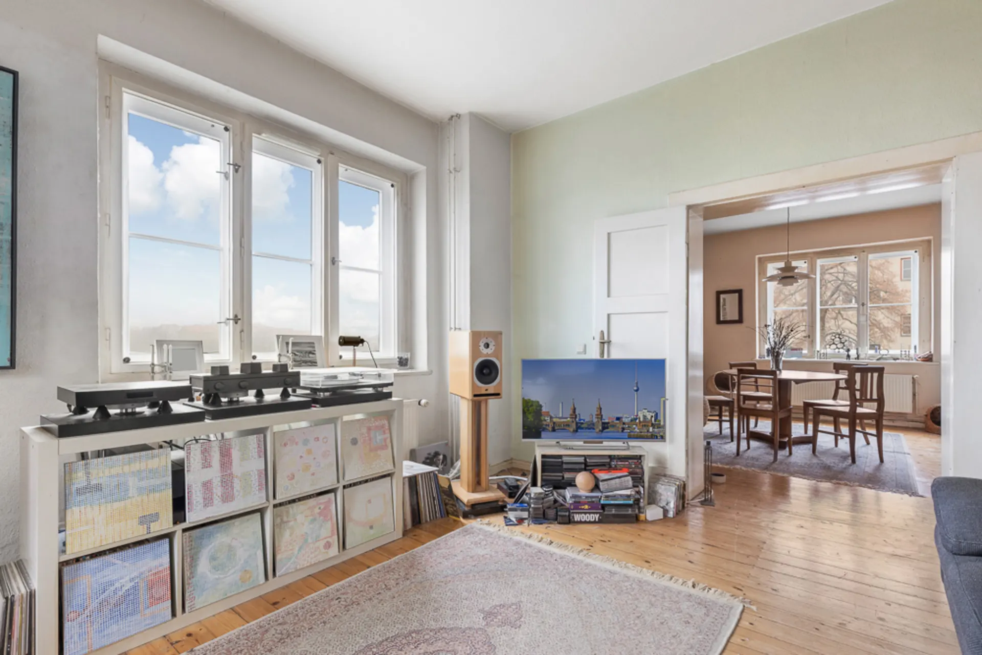 Helles Wohnzimmer mit großen Fenstern, Plattenspielern, Regalen und Blick auf ein Esszimmer.