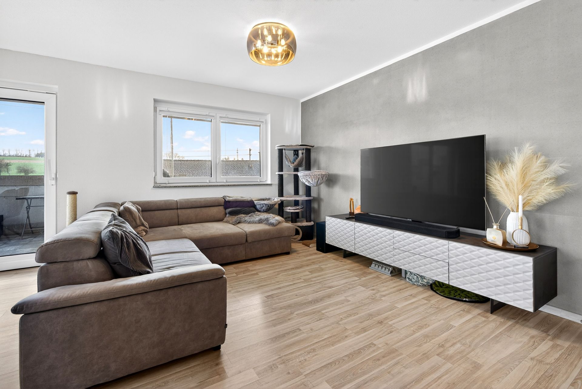 Modernes Wohnzimmer mit Ecksofa, großem Fernseher und Zugang zum Balkon.