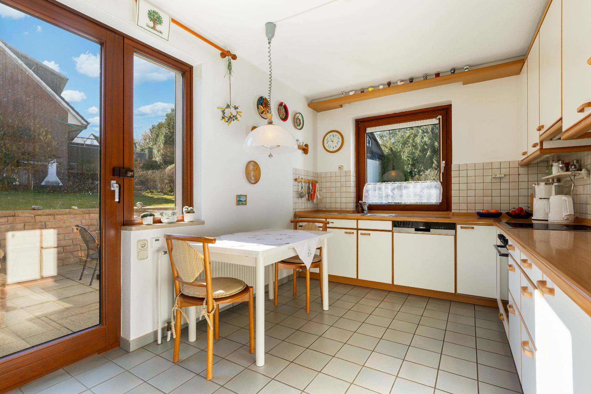 Helle Küche mit Esstisch, zwei Stühlen und Blick auf den Garten durch große Fenster.