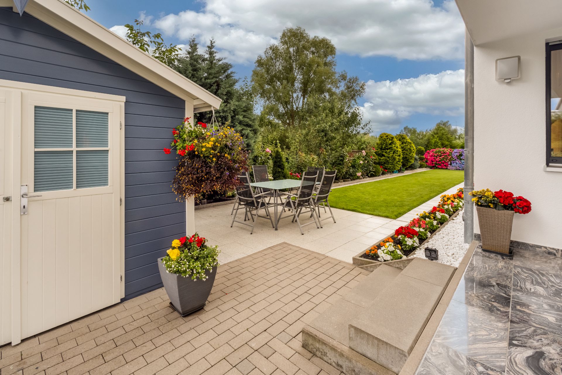 Gepflegter Garten mit Terrasse, Gartenhaus, Sitzgruppe und vielen bunten Blumen.