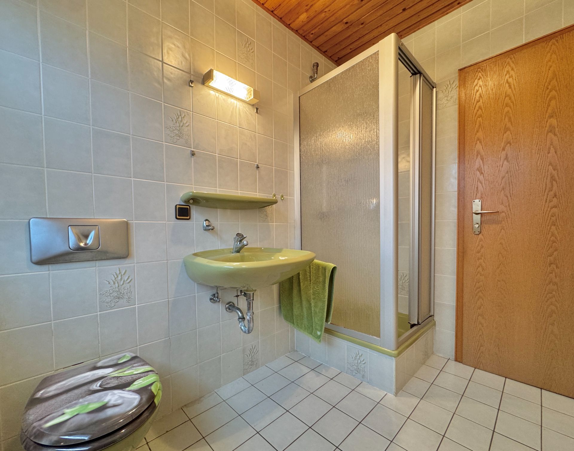 Badezimmer mit Duschkabine, Waschbecken, WC und Holzdecke.