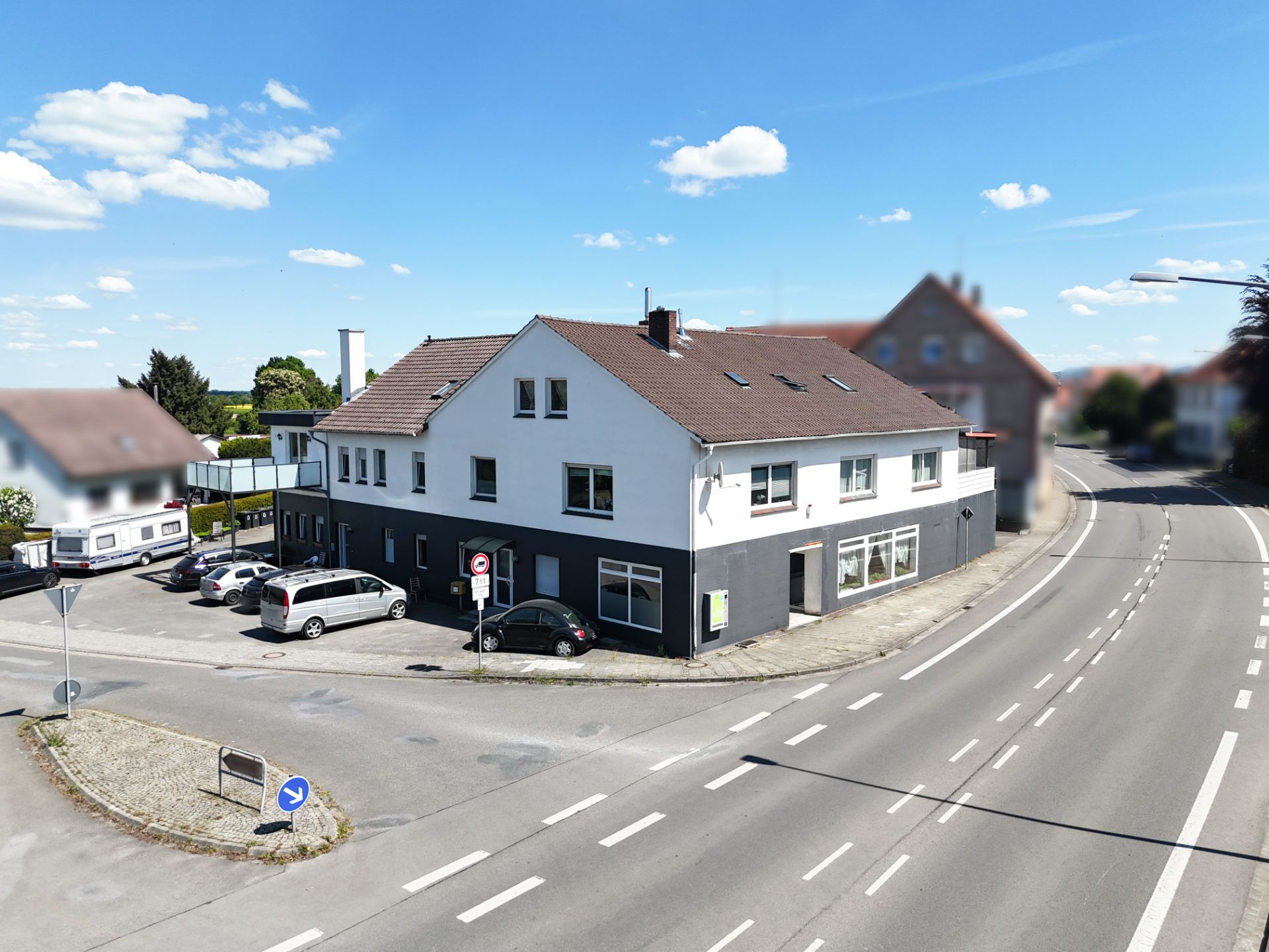 Zweistöckiges Wohnhaus an einer Straßenecke, mehrere geparkte Autos davor.