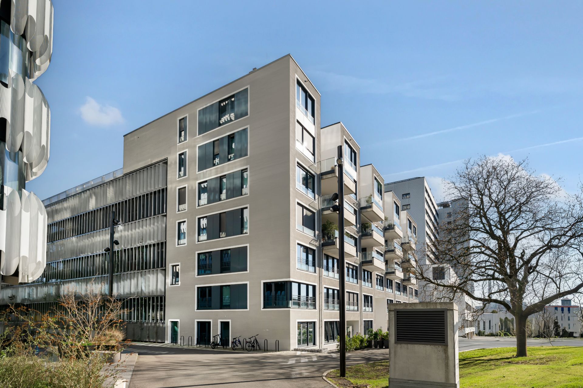 Mehrstöckiges Wohngebäude mit großen Fenstern und umliegender Grünfläche bei Tageslicht.