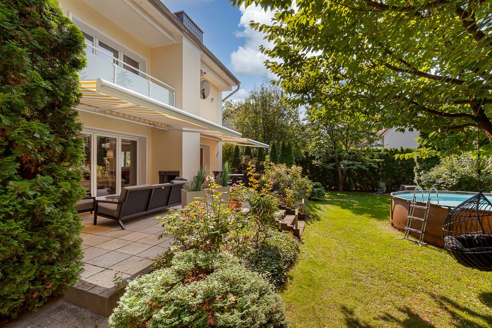 Garten mit Terrasse, Gartenmöbeln, Sonnenschutz und rundem Aufstellpool neben einem Wohnhaus.