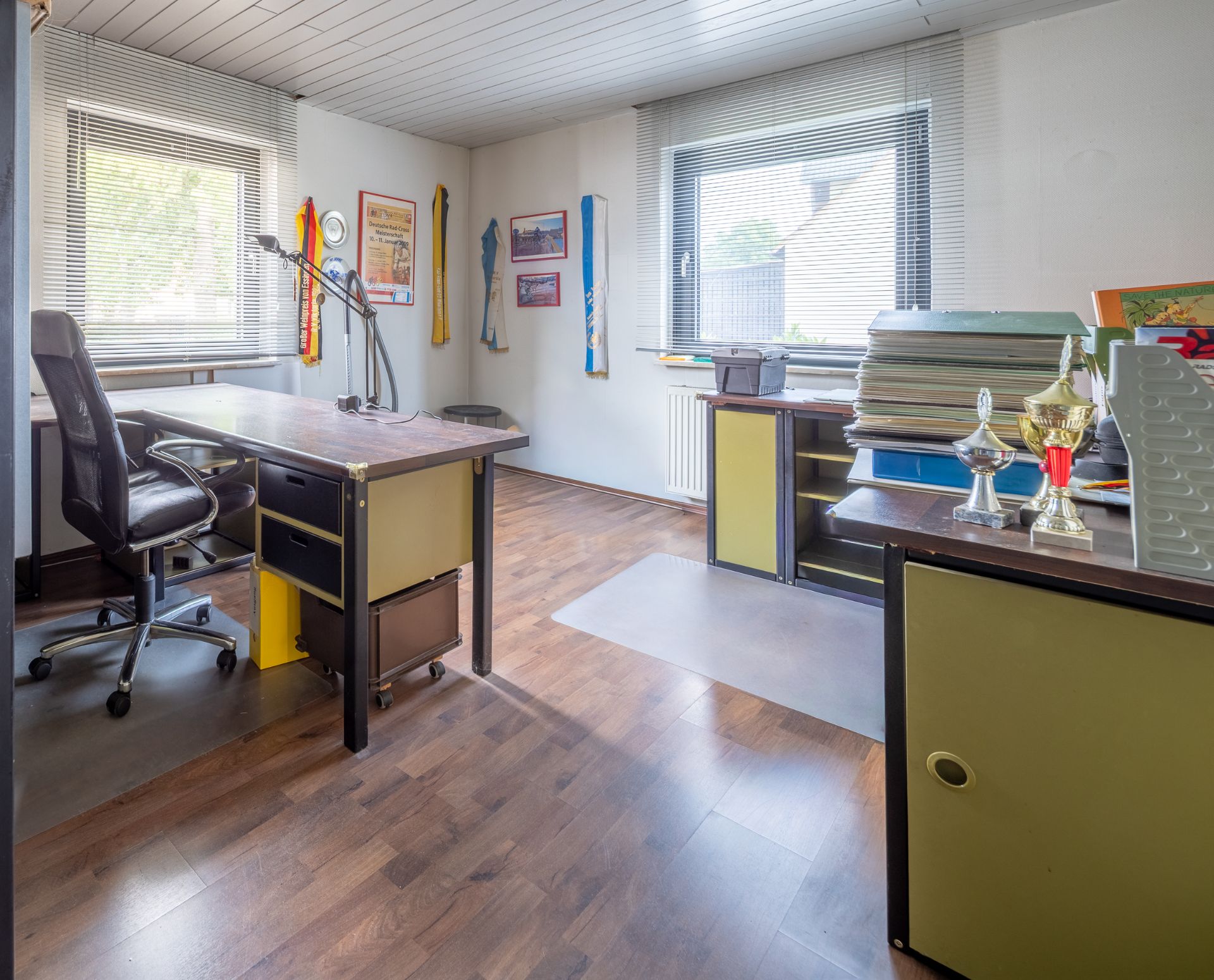 Helles Arbeitszimmer mit zwei Schreibtischen, Regalen, Stuhl und großen Fenstern.