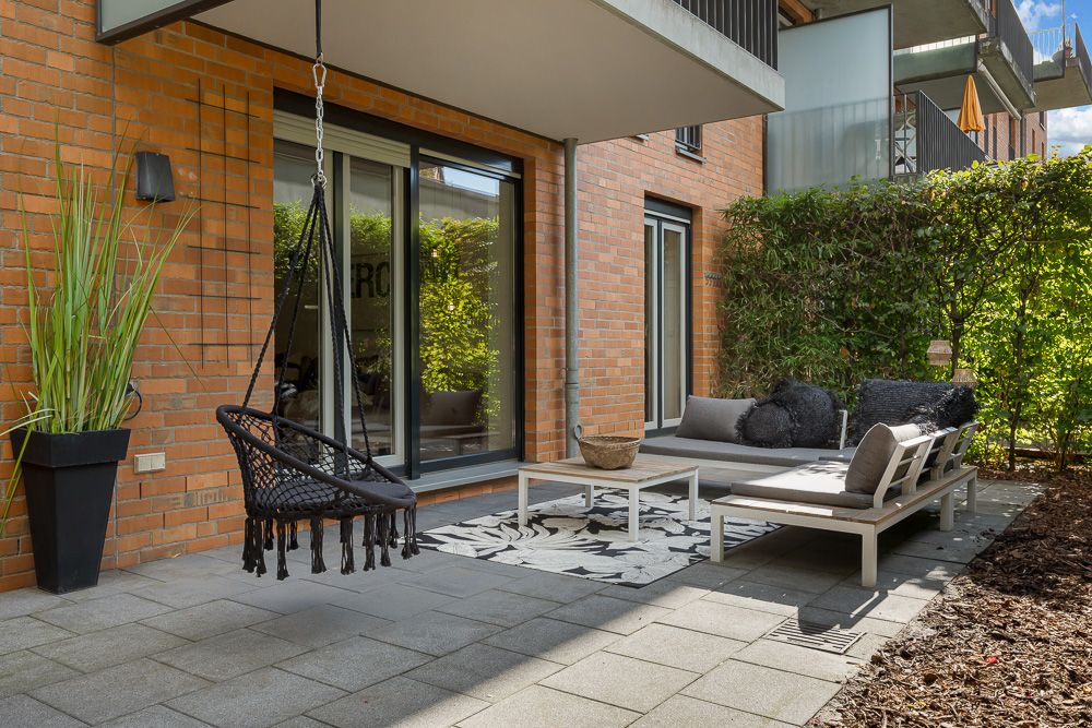 Moderne Terrasse mit Hängesessel, Sofa, Couchtisch und Pflanze vor einer Backsteinwand.