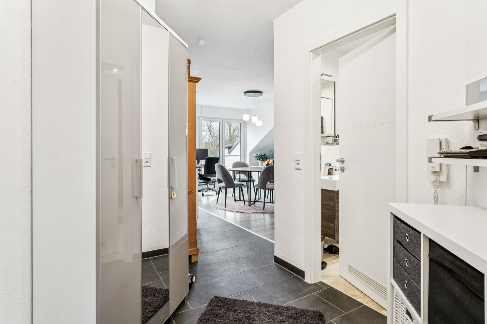 Heller Flur mit Blick ins Wohnzimmer und Essbereich, rechts ein Badezimmer.