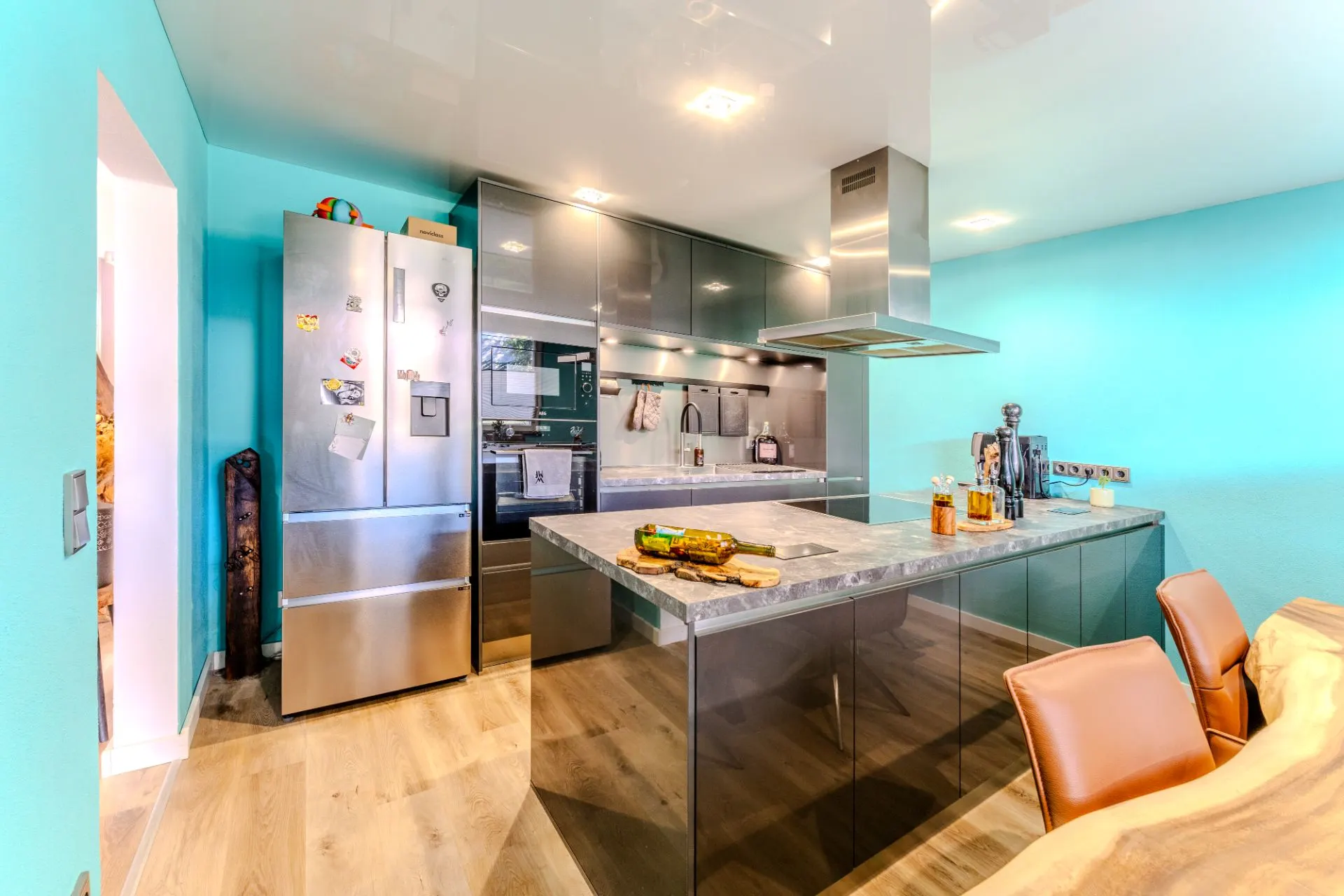 Moderne Küche mit Kücheninsel, Edelstahlkühlschrank und türkisfarbigen Wänden.