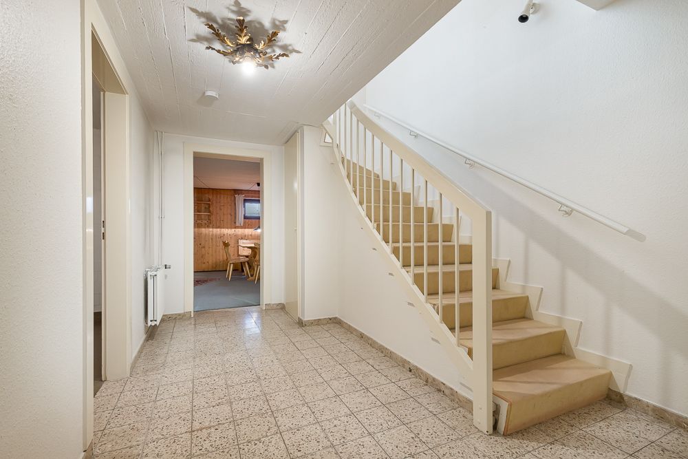 Heller Flur mit gefliesten Boden, Treppe nach oben und Zugang zu einem weiteren Raum.
