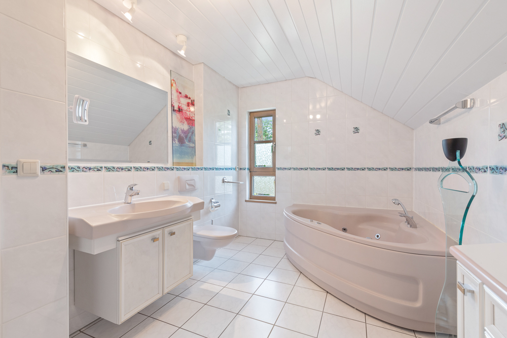 Modernes Bad mit Eckbadewanne, Doppelwaschbecken, WC und großem Spiegel unter Dachschräge.