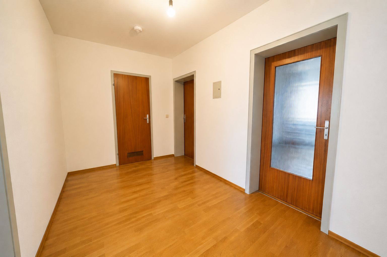 Leerer Flur mit Parkettboden und drei Holztüren in einer Wohnung.